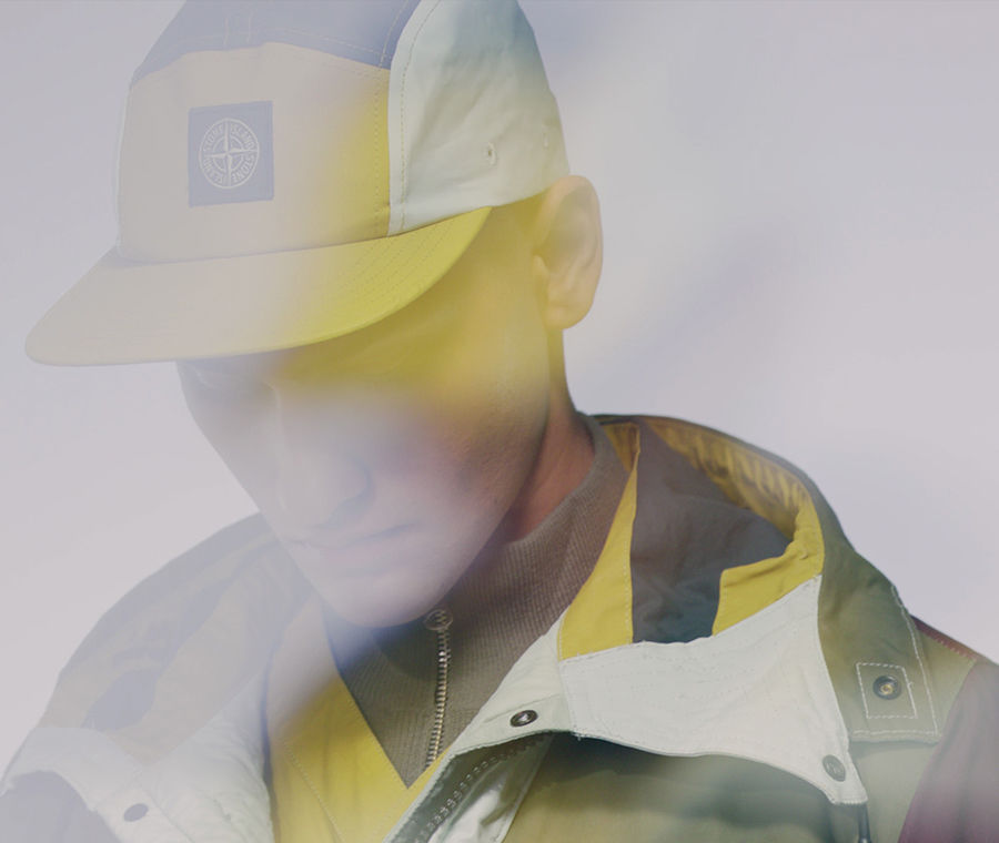 Close up of model wearing multicolored jacket and matching cap wit Stone Island patch.