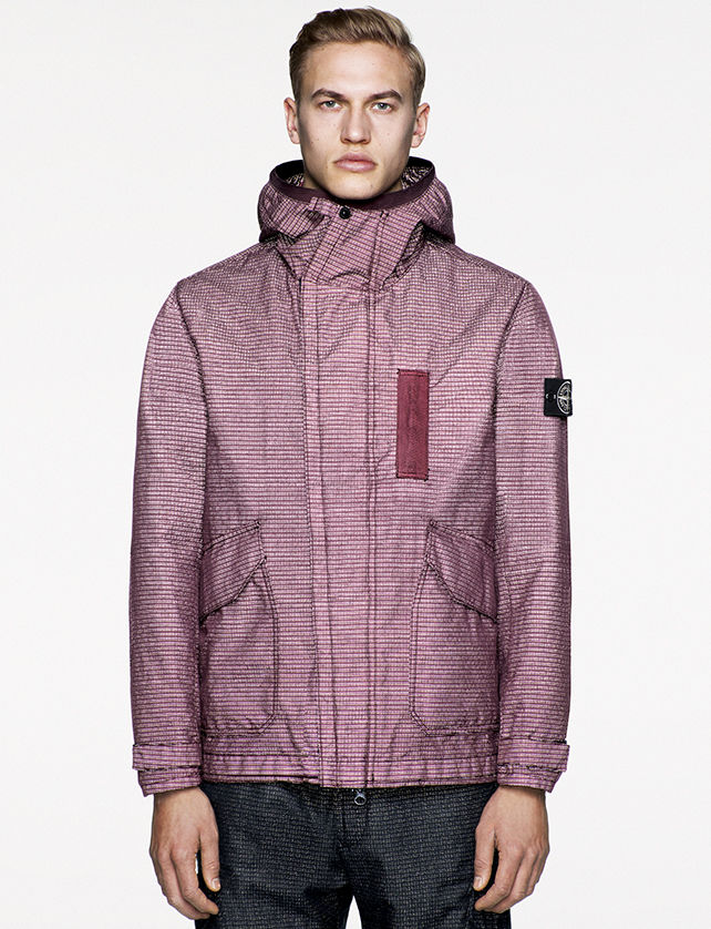 Model wearing maroon jacket in jacquard fabric with high collar, large diagonal flap pockets and concealed fastening.