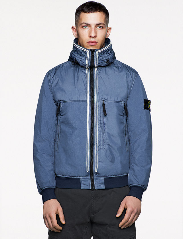 Model wearing blue bomber jacket with high collar, three vertical zipper pockets and zipper closure.