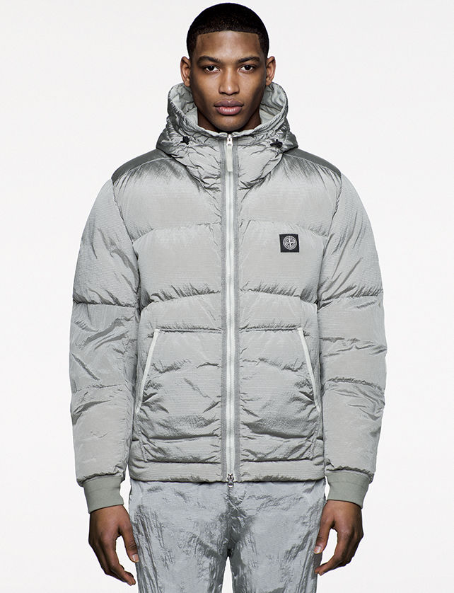 Model wearing shiny gray, quilted jacket with hood, diagonal pockets and zipper closure.