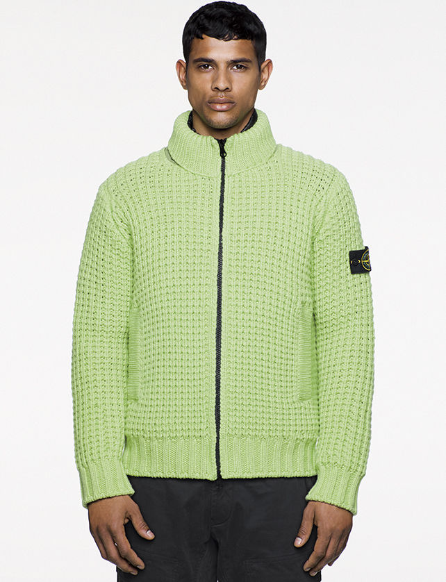 Model wearing green knitted cardigan with stand up collar, vertical pockets and black zipper fastening.