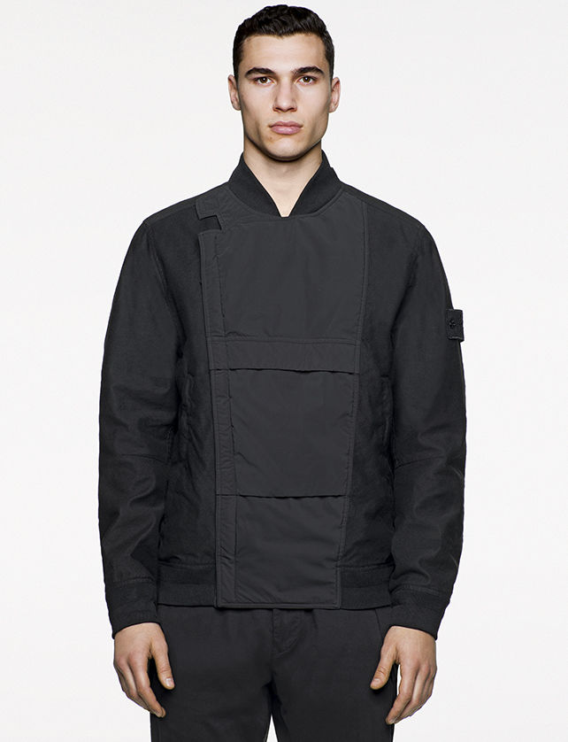 Model wearing black bomber jacket with a dark gray central panel and off center, concealed fastening.