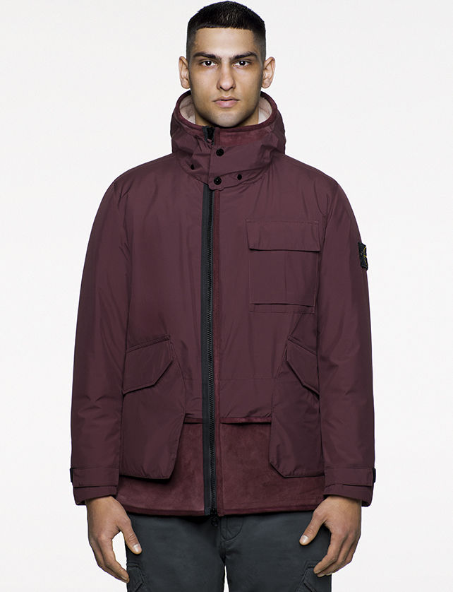 Model wearing maroon jacket with stand up collar, large diagonal bellows pockets and off center zipper fastening.