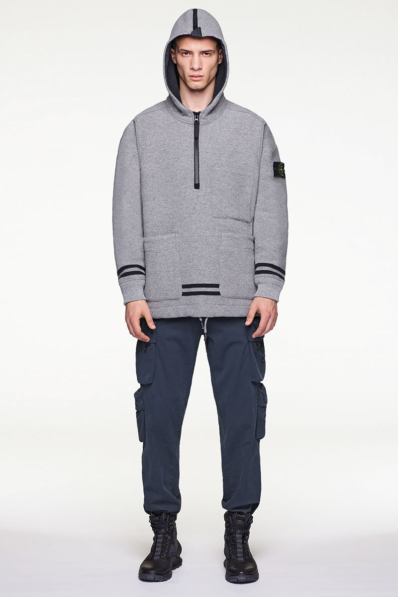 Front view of model wearing gray hooded sweater with dark stripes, blue pants and black and blue high top sneakers.