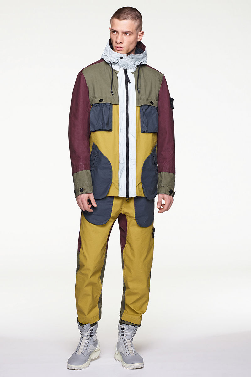 Front view of model wearing multi colored parka with white hood, matching pants and high top sneakers.
