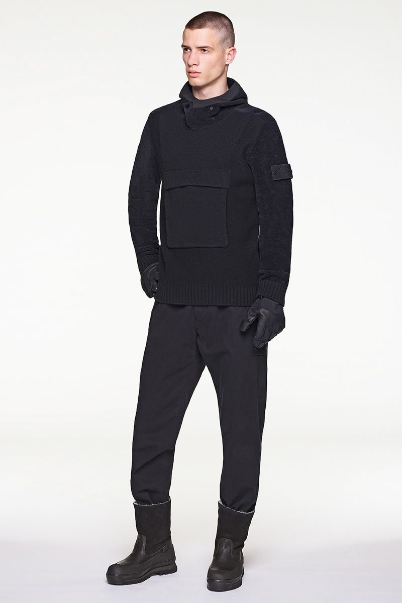 Model wearing black hoodie with central pouch pocket, black pants and black boots.