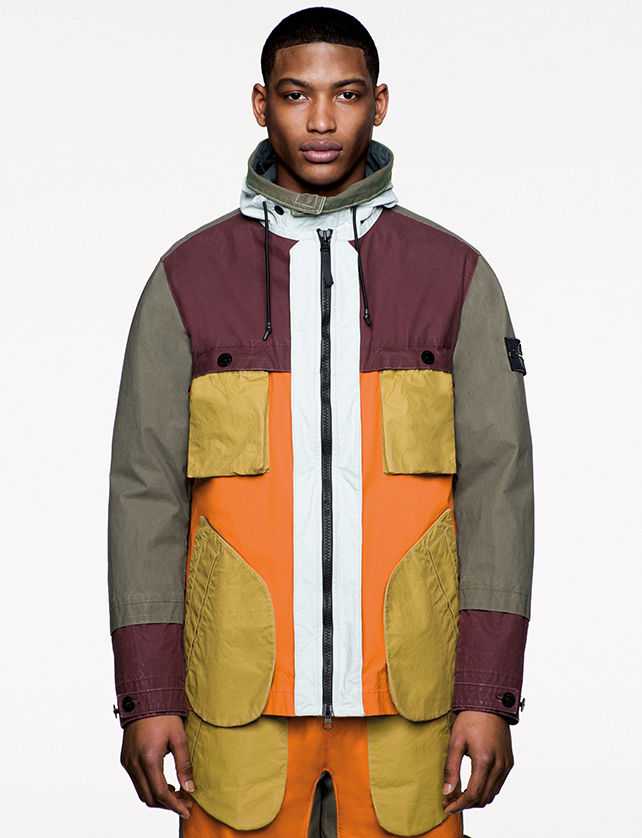 Model wearing multi colored jacket with large diagonal bellows pockets and matching pants.