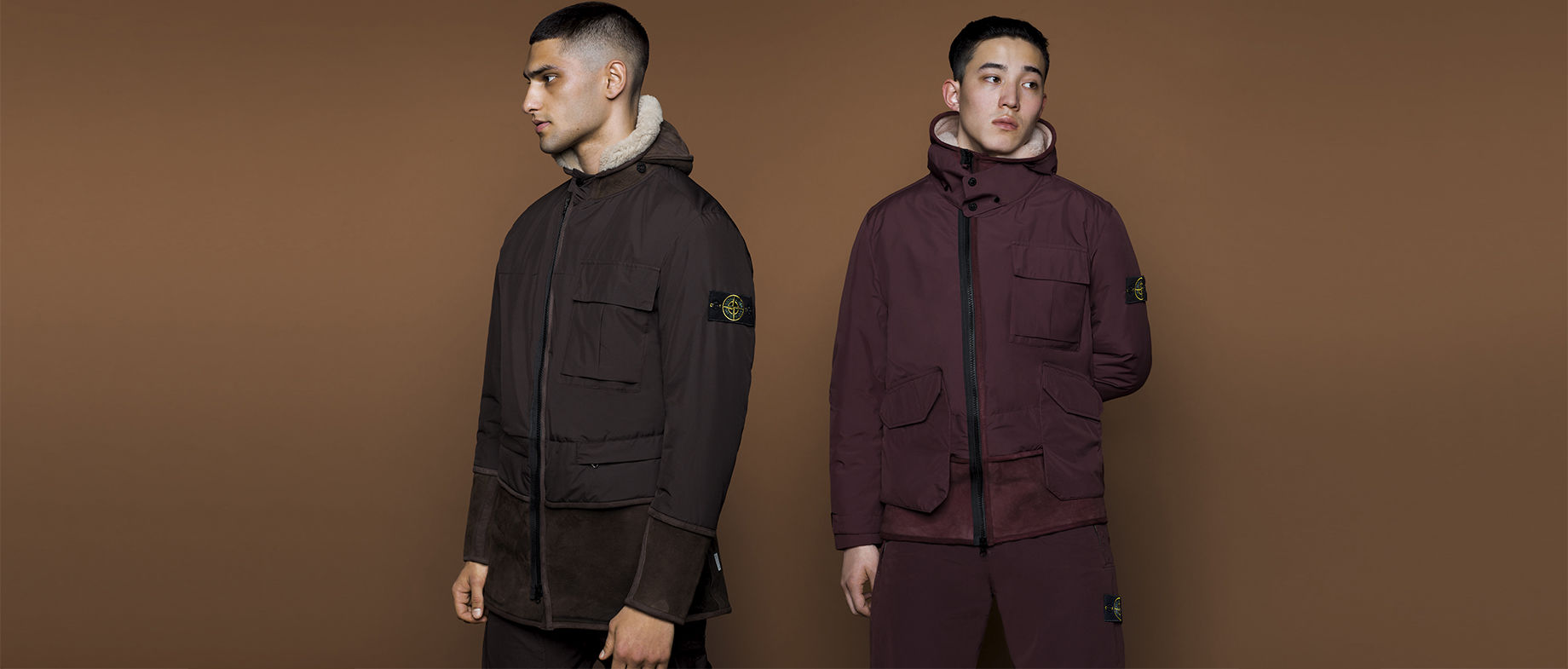 Two models wearing hooded parkas with patch pockets and black zippers, one in dark brown and one in burgundy