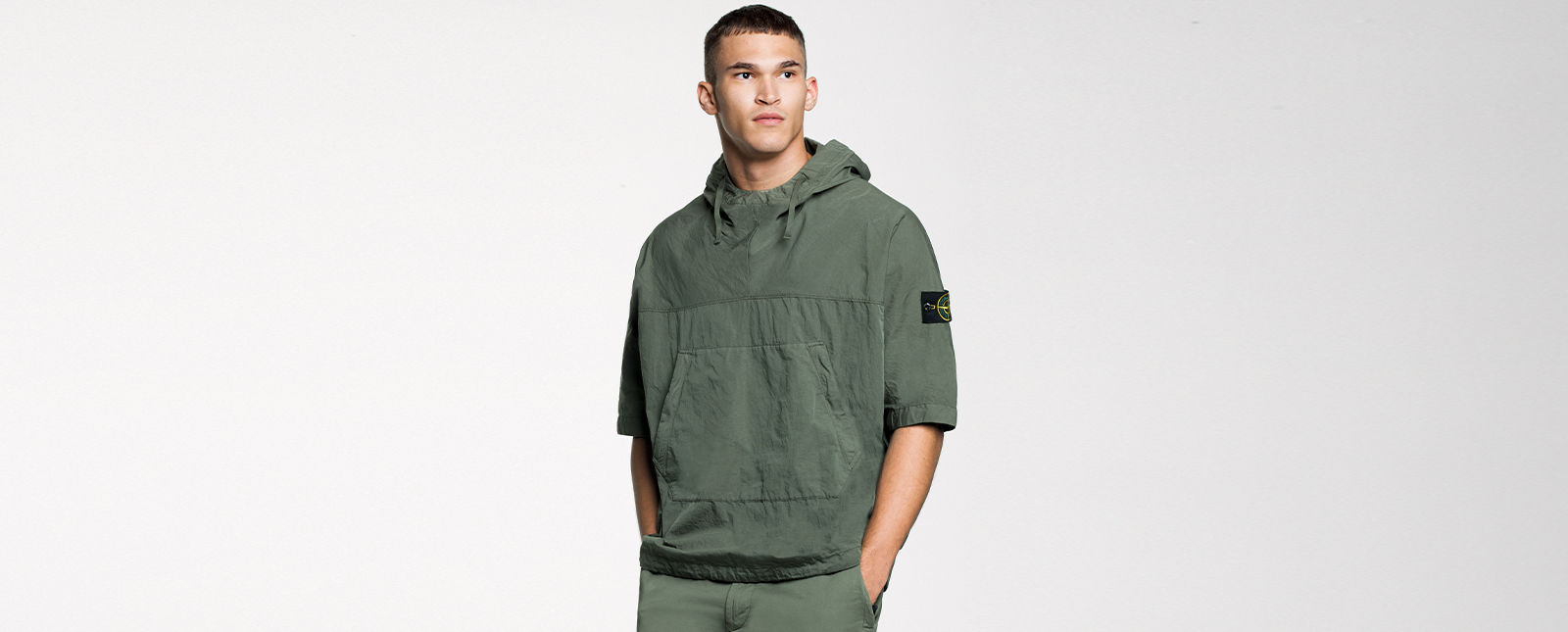 Model wearing a green short sleeved hooded overshirt with central pouch pocket and the Stone Island badge on the left sleeve.