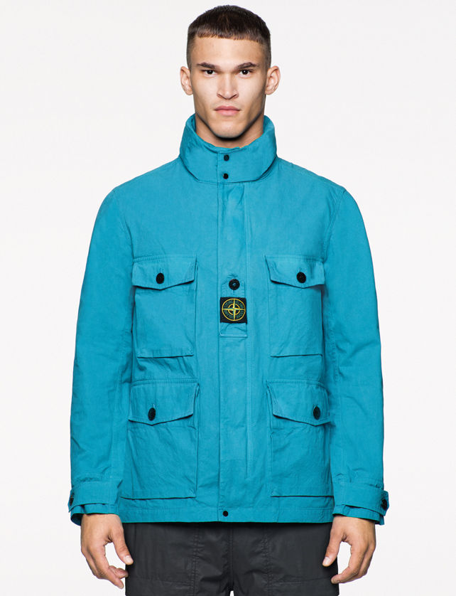 Model wearing a bright blue jacket with stand collar, four flap pockets on the front with black buttons, Stone Island patch in the center of the chest
