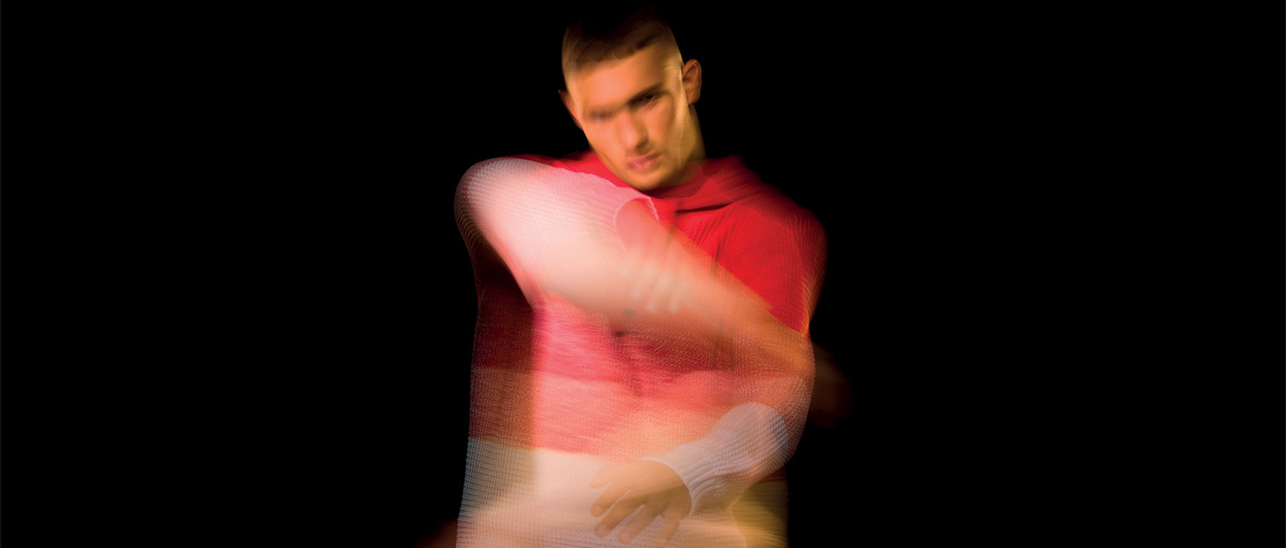 Model standing in shadow wearing a collared shirt jacket and a cap with the Stone Island compass rose.