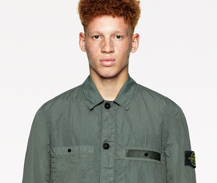 Model wearing a green shirt jacket with collar, black button closure, buttoned chest pockets, side pockets, and white pants