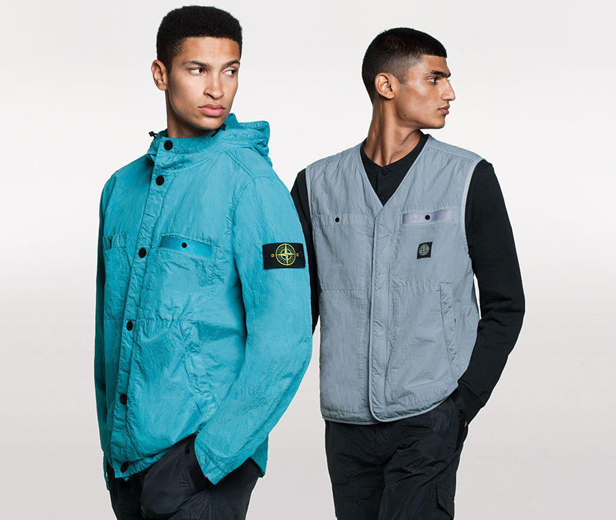 Two models, one wearing black pants and a bright blue hooded jacket with button closure, two patch pockets and two side pockets, the other one wearing black pants, a black shirt and a gray V neck vest with two patch pockets and two side pockets.