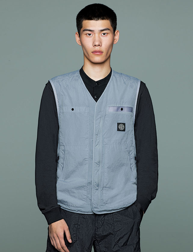 Model wearing black pants, a black shirt and a gray V neck vest with two patch pockets and two side pockets.
