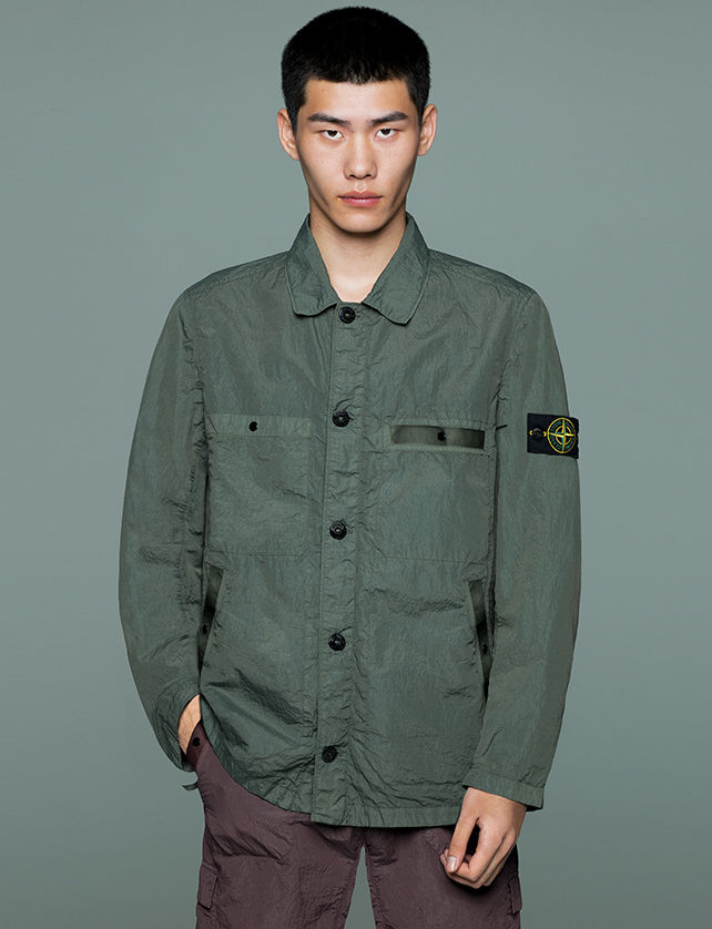 Model wearing dark brown pants and a military green jacket with collar, button closure, two patch pockets and two side pockets.