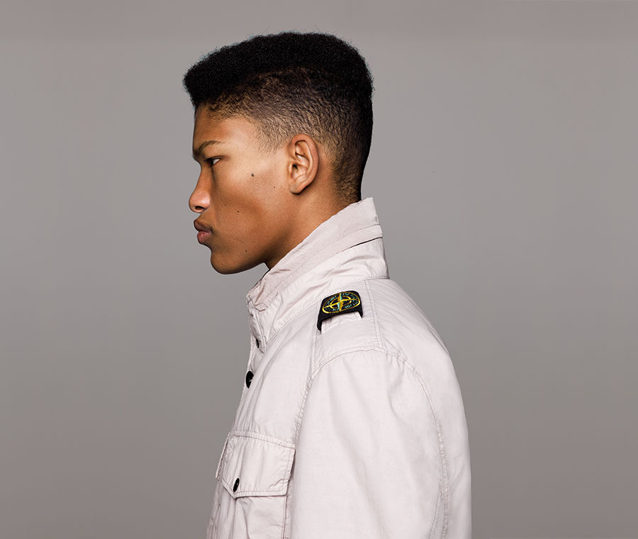 Side view of model wearing an off white jacket with standing collar, bellows chest pocket with flap and snap fastening and Stone Island badge on left shoulder.