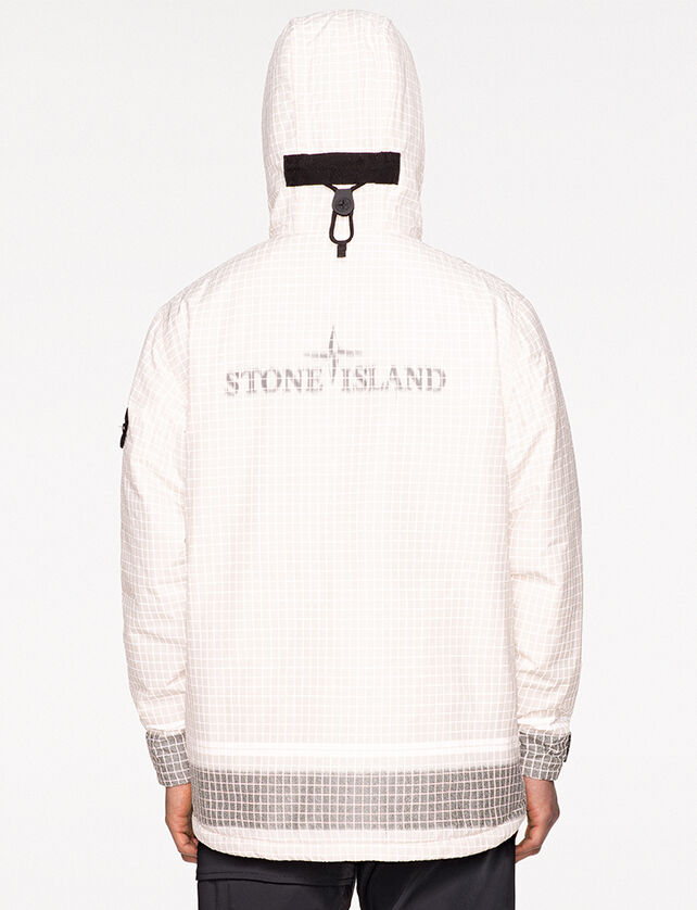Back view of model wearing black pants and a white check print anorak with hood up, showing a black toggle, Stone Island logo at the center of the back and gray colored cuffs and bottom hem.