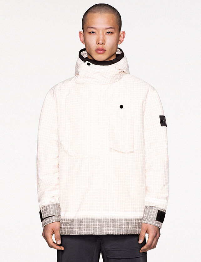 Model wearing dark colored pants and a white check print anorak with hood and light gray colored cuffs and bottom hem.