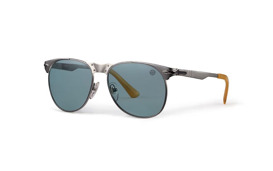 Still life image of a pair of sunglasses with gray metal frame, a large metal bridge with tiny screws, adjustable nosepads, dark orange acetate temple tips and drop shape lenses, one with a small Stone Island compass rose logo in the top corner.