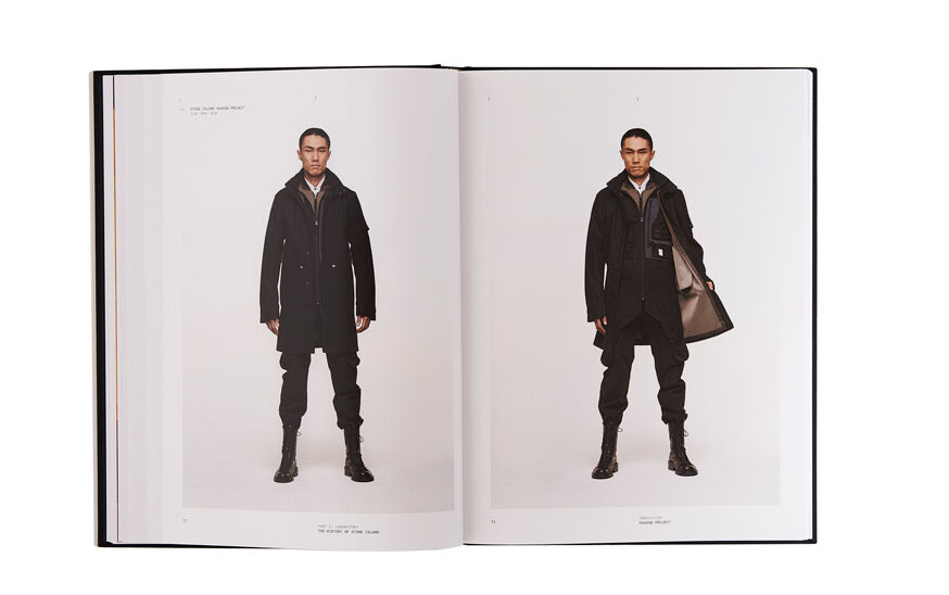 Still life image of an open hardcover book showing a picture of a model wearing black boots, pants and long jacket on the left page and the same model in the same outfit showing the internal lining of the jacket on the right page.