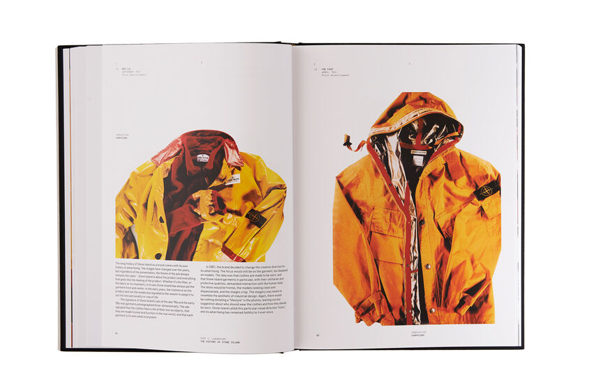 Still life image of an open hardcover book showing printed text and a still life image of a dark yellow jacket with red details on the left page and a still life image of a dark yellow hooded jacket with silver lining on the right page.