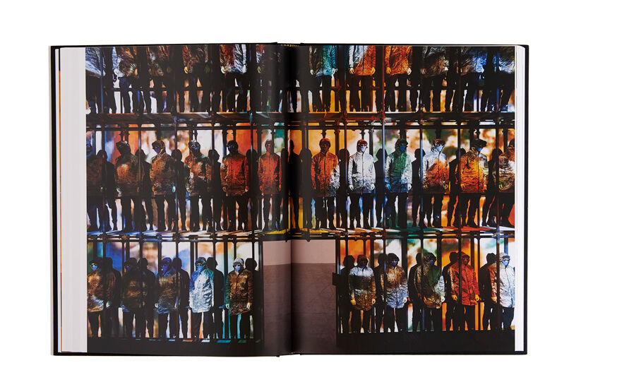 Still life image of an open hardcover book showing across both pages a picture of an installation of many mannequins wearing hooded jackets.