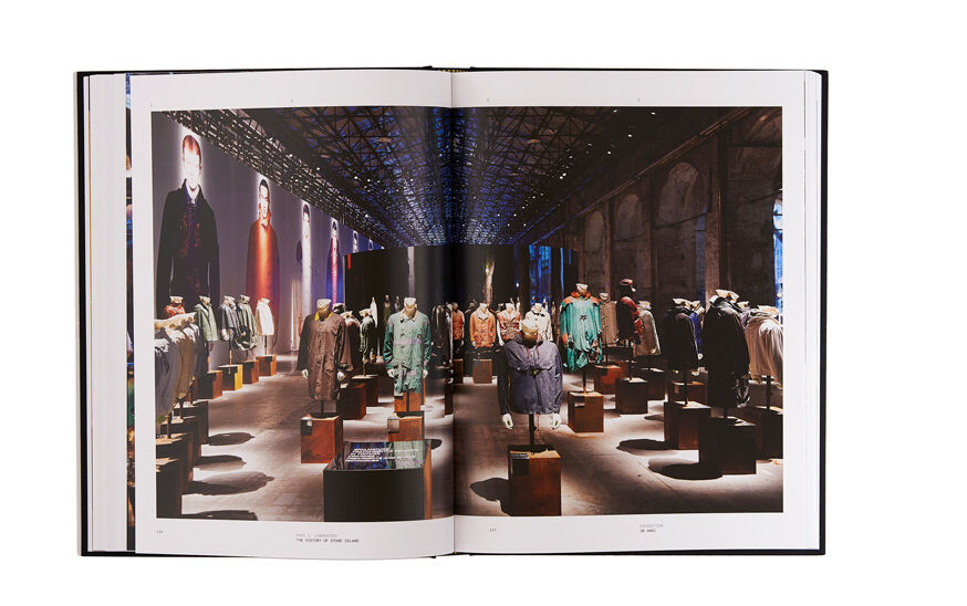 Still life image of an open hardcover book showing across both pages a picture of an installation of many mannequins wearing jackets in different colors and styles.