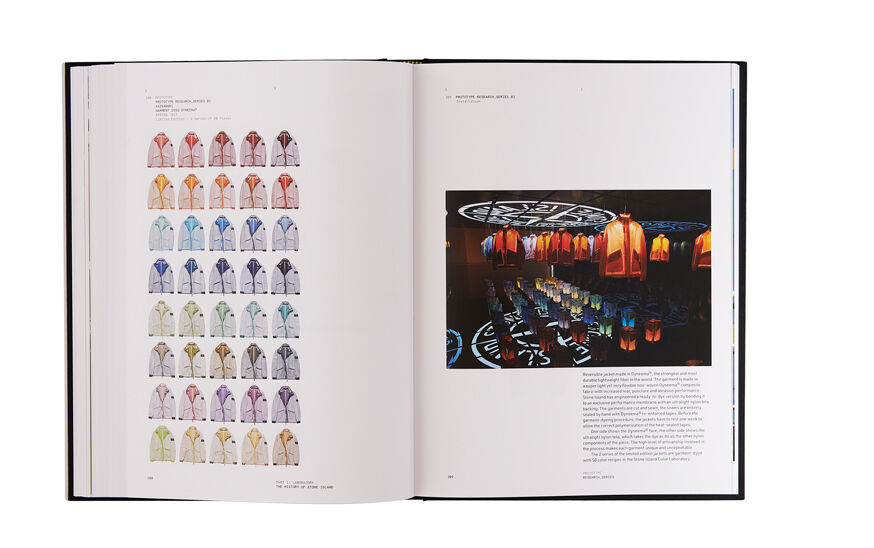 Still life image of an open hardcover book showing printed text and jackets in a variety of colors on the left page and printed text and an installation with jackets of different colors hanging from the ceiling on the right page.