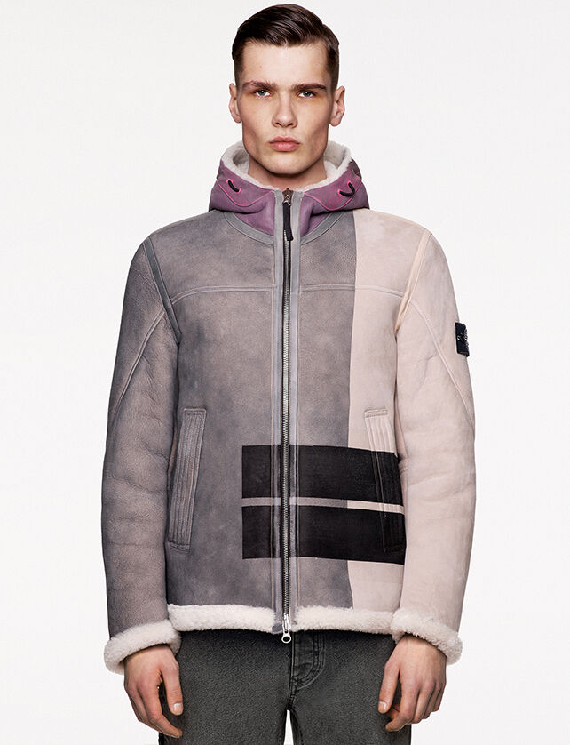 Model wearing burgundy check and paint splatter print pants and a matching anorak with standing collar, front hand pockets with flap and central buttoned strap bearing the Stone Island badge.