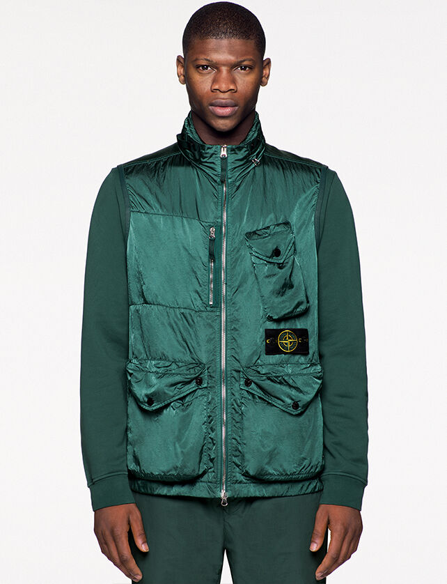 Model wearing dark green pants, a matching sweatshirt and a green shiny effect vest with standing collar, two way zipper fastening, one bellows chest patch pocket on the left side with a triangular flap and snap, one vertical chest pocket with zipper, the