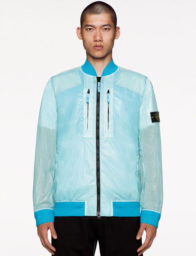 Model wearing black pants and a light blue see through bomber jacket with shiny effect, two way black zipper fastening, two vertical chest pockets with zipper and the Stone Island badge on the upper left arm.