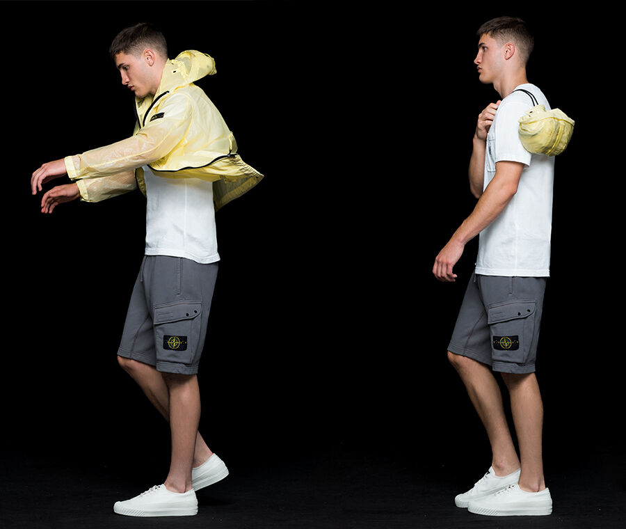 Four shots of the same model wearing gray cargo shorts, a white crewneck T shirt and a yellow see through hooded jacket with shiny effect, showing that the jacket is pocketable and can be stored in a carrying pouch.
