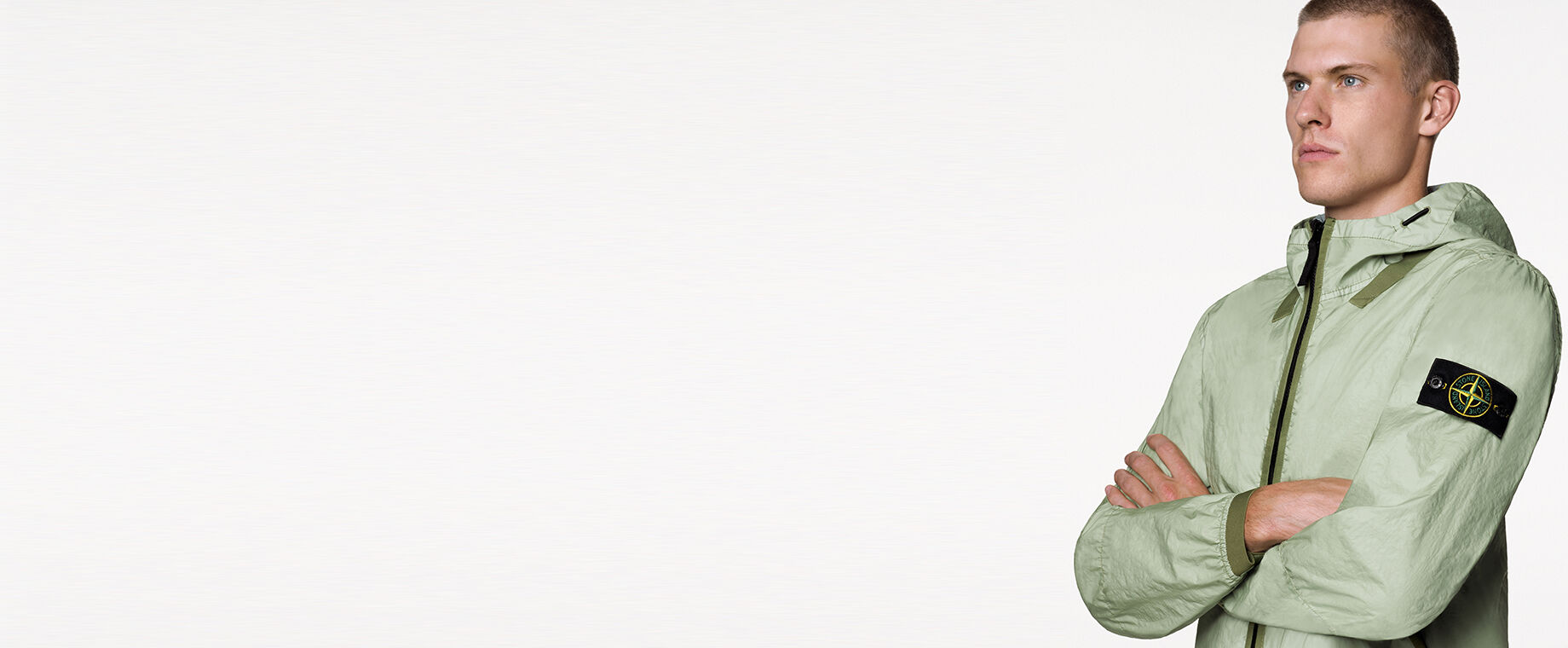 Close up of model wearing a light green jacket with darker green edging details, hood with drawstring, black zipper fastening and the Stone Island badge on the upper left arm.