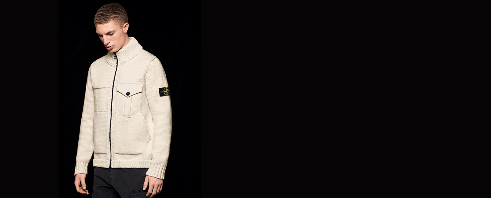 Model wearing black pants and an off white knit sweater with two way zipper fastening, one chest pocket with flap, ribbed cuffs, bottom hem and collar and the Stone Island badge on the upper left sleeve.