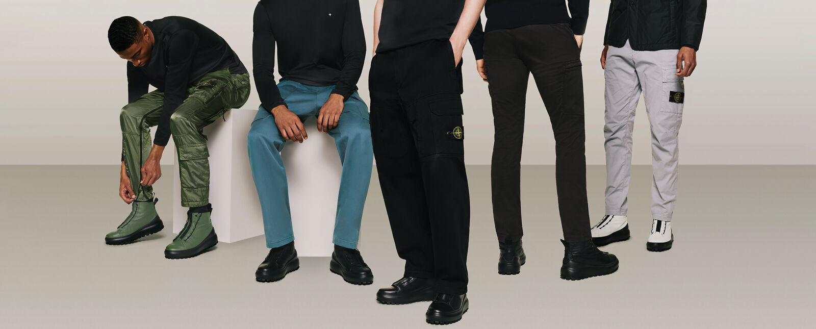 Five models wearing black tops and cargo pants in different styles and colors, shiny green, teal blue, black and light gray.