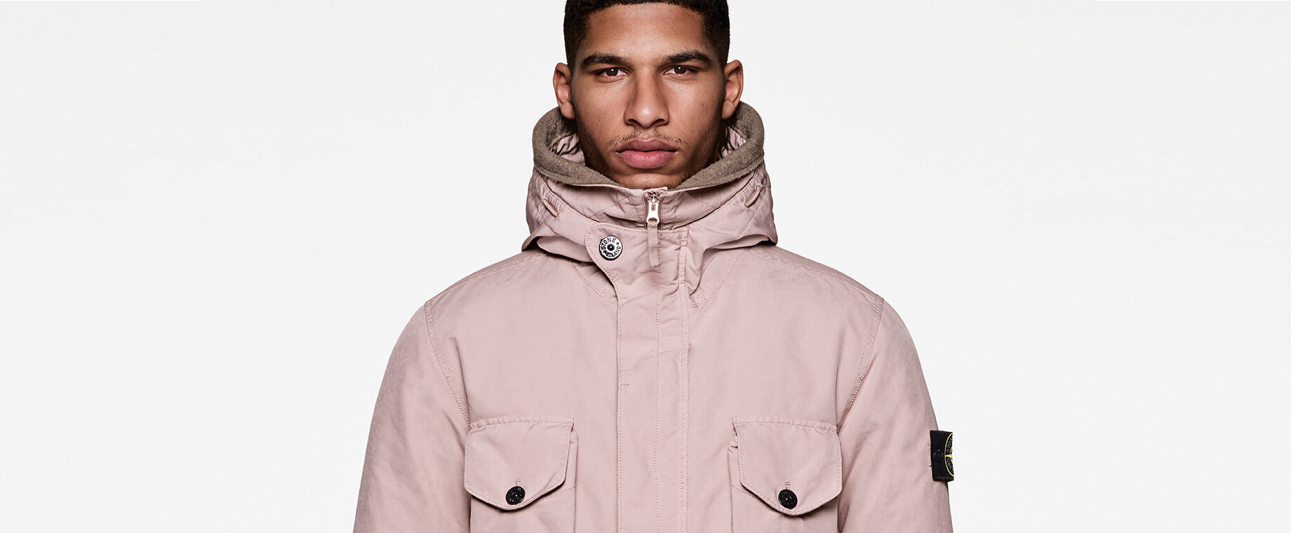 Model wearing a light pink hooded jacket with concealed full-zip fastening, four buttoned flap pockets and the Stone Island badge on the upper left sleeve.