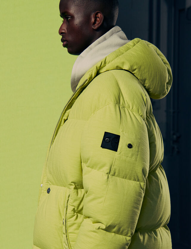 Model wearing a bright green padded jacket with the Shadow Project badge on the sleeve.