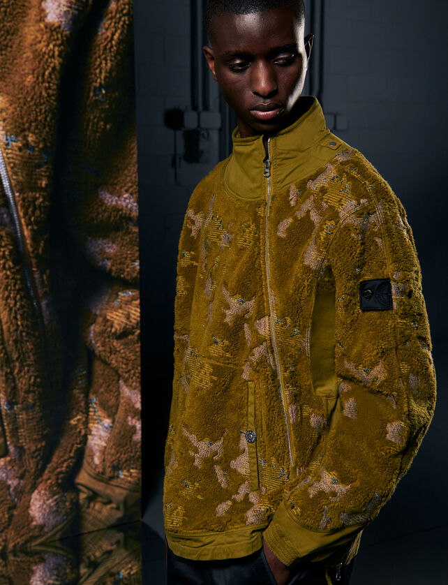 Model wearing a yellow fleece jacket beside a tall screen with a close-up of the outfit.