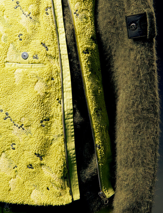 Close-up of a yellow fleece vest jacket with textured camo pattern worn over a brown hoodie with Shadow Project badge on the sleeve.