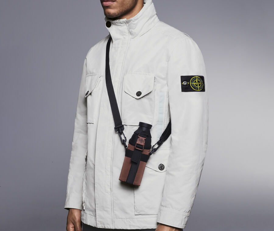 Model wearing an off-white jacket carrying a black canteen in a brown holster with a cross body strap.