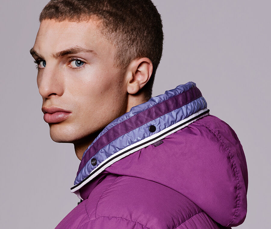 Close-up side view of model wearing a magenta hooded jacket with two-tone high collar and snap button detail.
