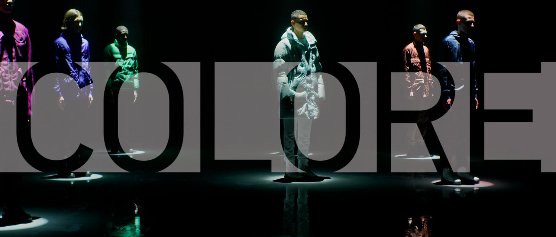 Six male models, each wearing a different colored outfit, stand beneath white spotlights with overlaid text that reads