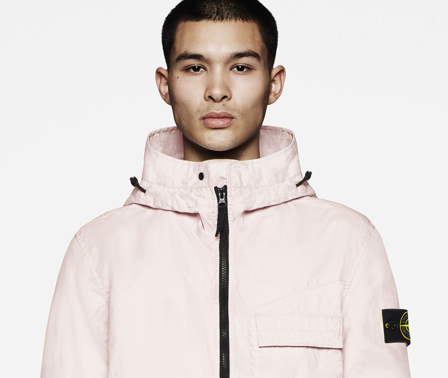 Model wearing a pink hooded jacket with black zipper, chest flap pocket and Stone Island badge on the upper sleeve.