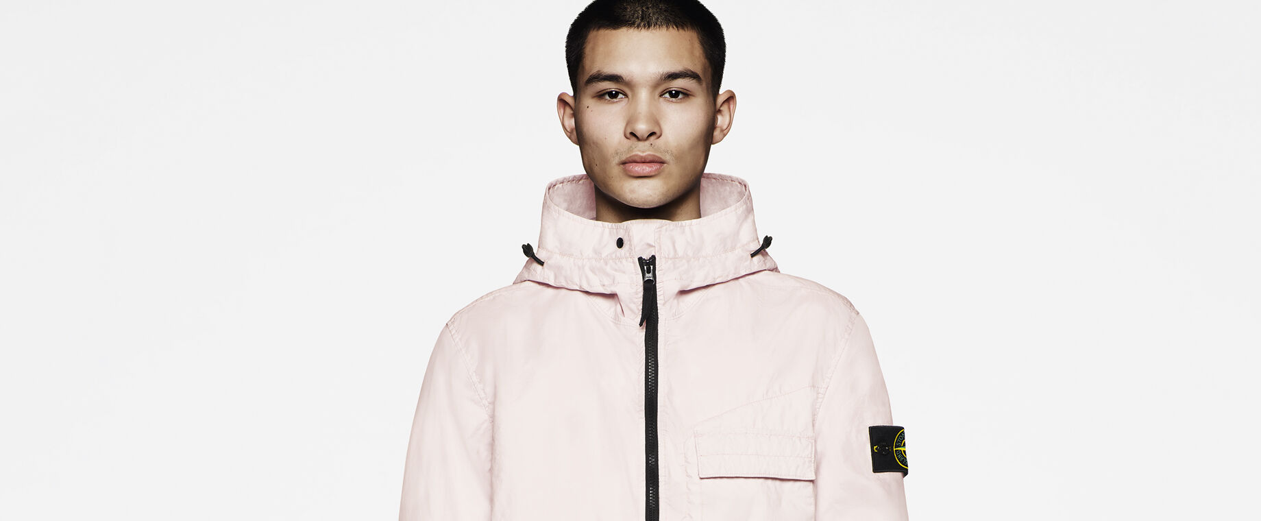 Model wearing a pink hooded jacket with black zipper, chest flap pocket and Stone Island badge on the upper sleeve.