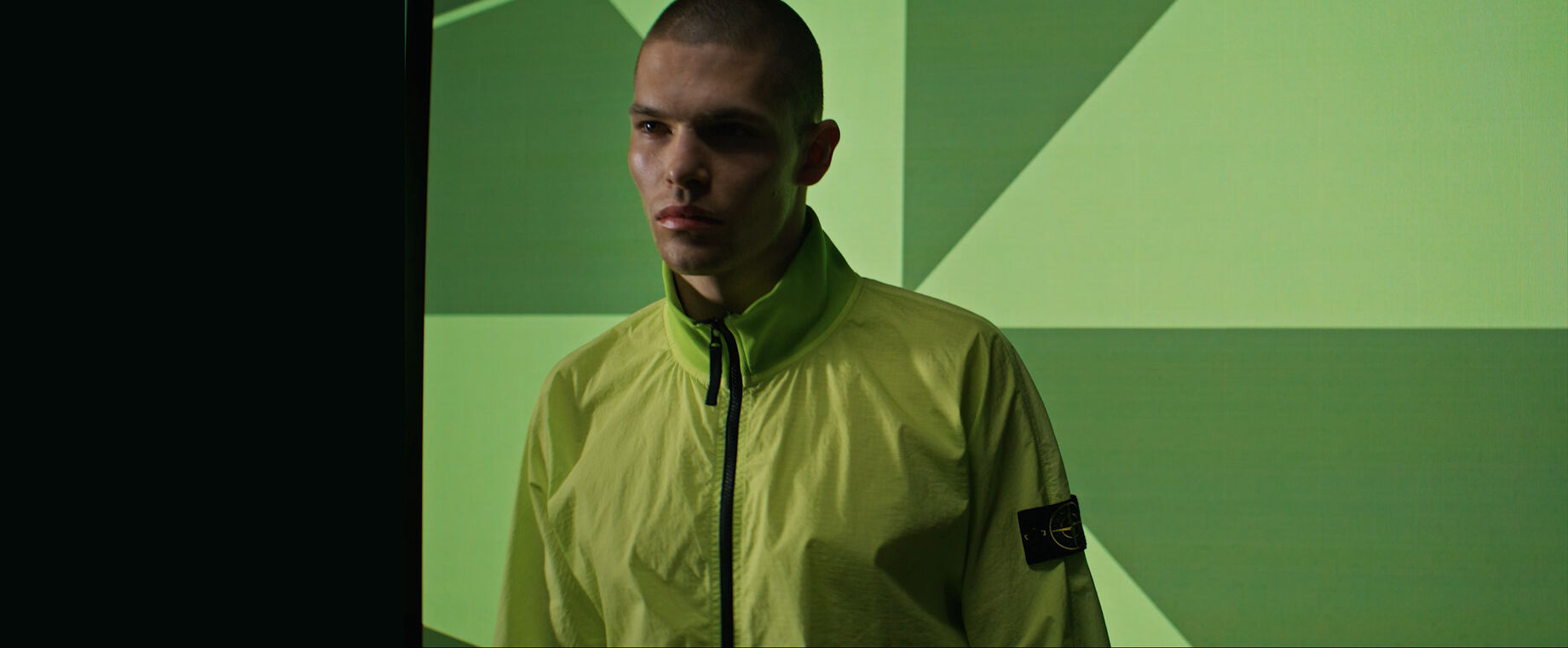 Headshot of a model wearing a green zipped jacket against a green two-tone graphic backdrop.
