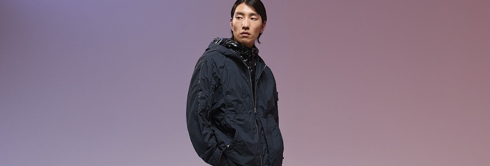 Model posed with hands in pockets wearing a black full-zip coat over a shiny-effect hooded jacket.