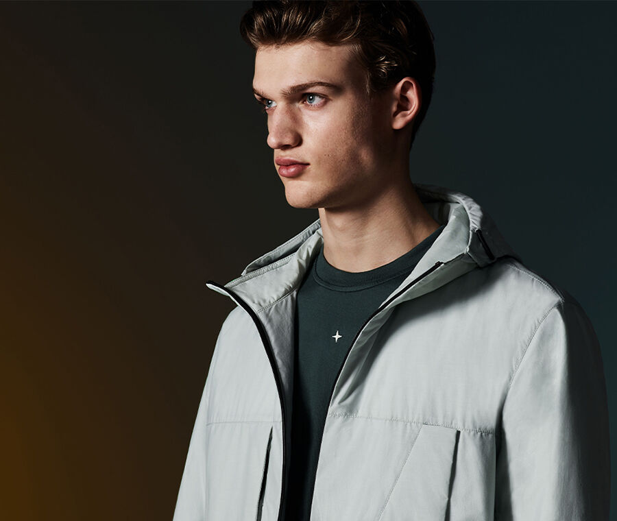 Close-up of model wearing a dark gray T-shirt with compass rose embroidery on chest and gray hooded jacket.