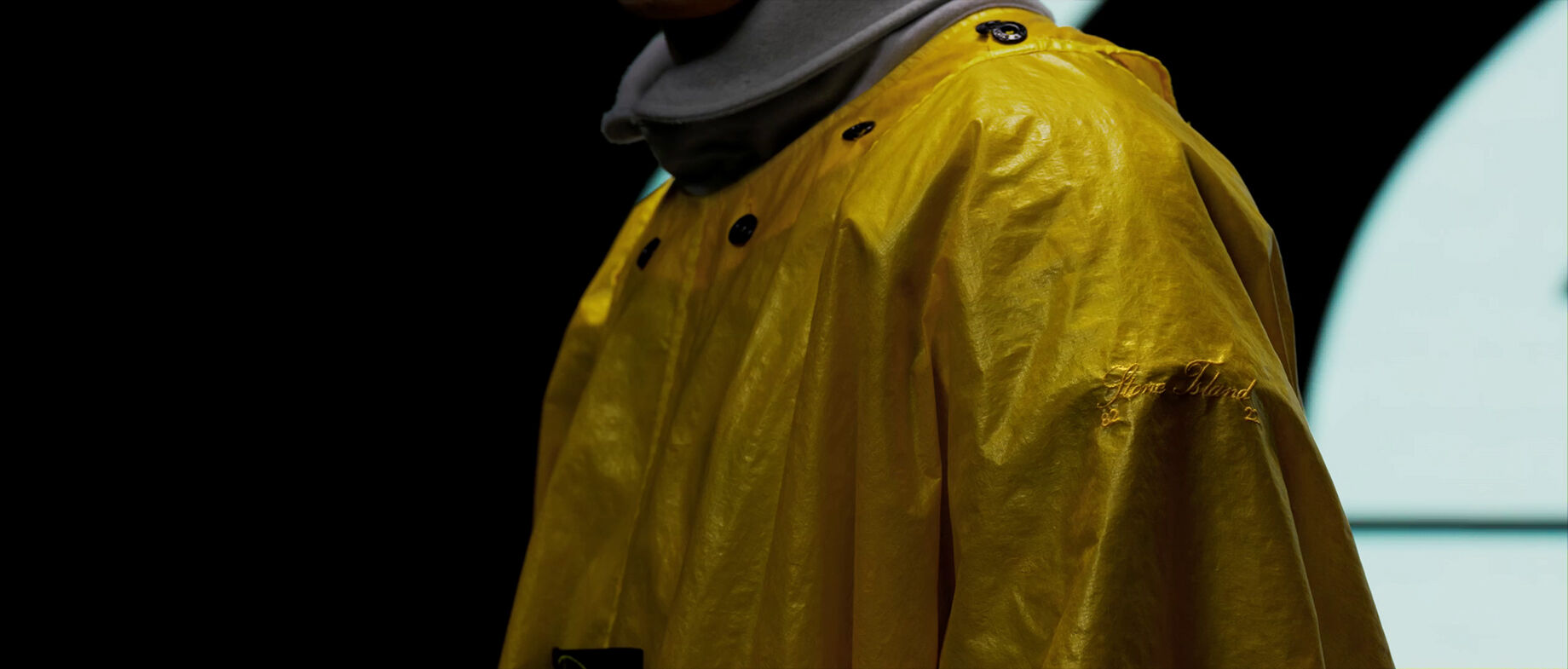 Close-up of yellow raincoat with Stone Island embroidery on sleeve.