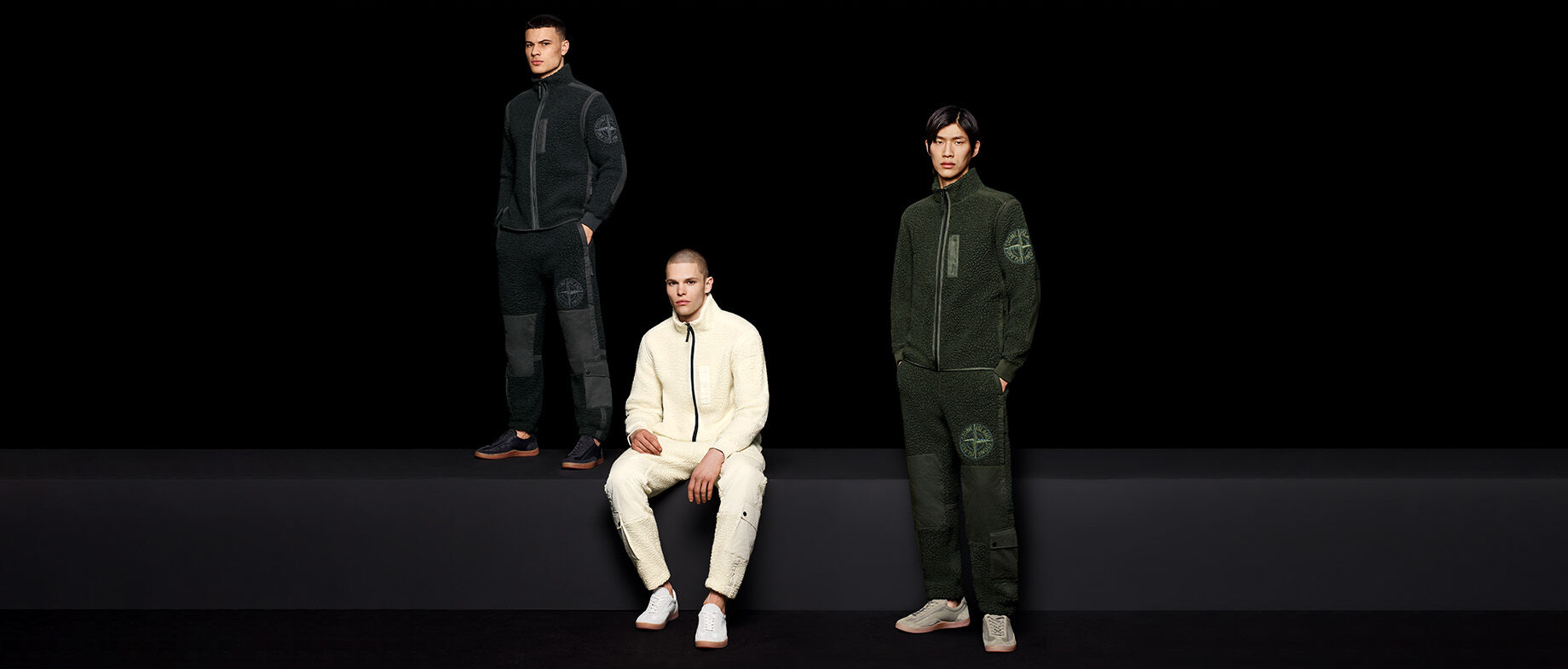 Three models wearing full-zip fleece sweatshirts and pants with Stone Island compass rose details.
