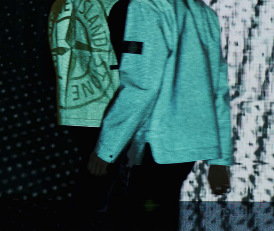 Video still featuring reflective jackets with Stone Island badge and compass rose print.